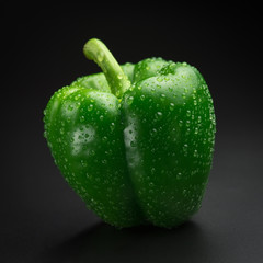 Green pepper with water drops on a black background. Fresh bright colorful peppers on a black background