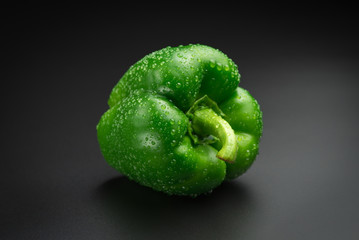 Green pepper with water drops on a black background.
