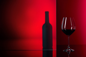 Bottle and glass of red wine on a red background.