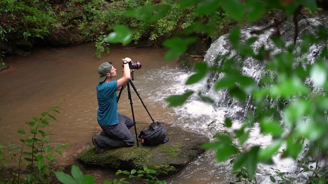 Idyllic scene of a photographer taking a picture of a natural waterfall in the lush forest - slow motion