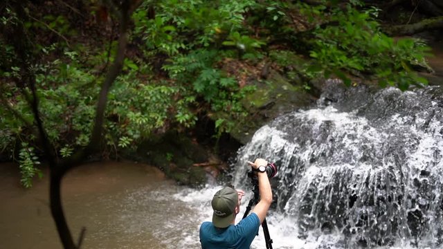 Young male photographer using a tripod and camera to photograph a waterfall - slow motion