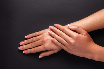 The hands of a young girl are covered with a highlight top. French manicure. Hands on a black...