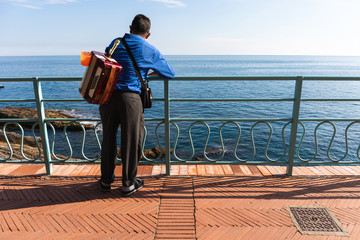Italian street musician standing at railing at beach promenade