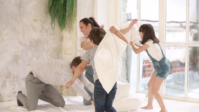 Family with little kids play fight with pillows at home