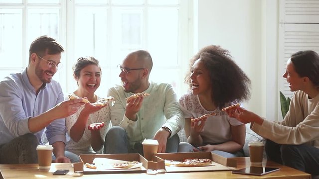 Overjoyed cheerful diverse friends gather together eating pizza enjoy conversation