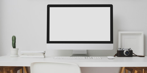 Modern workspace with blank screen desktop computer and decorations on white table and white wall