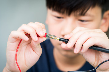 Smart looking Asian boy connecting a crocodile clip with multimeter negative probe. Science, Technology, Engineering and Mathematics (STEM) education concept.
