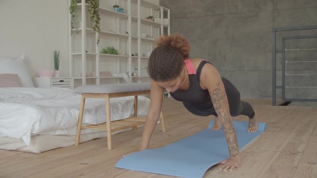 Motivated determined sporty fit african american woman on fitness mat doing plank static exercise for abdominal strength in domestic room. Concentrated female practicing pilates plank exercise indoors