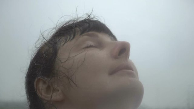 Woman looking up at rain in nature with wet hair. Slow motion. Girl smiles rain drops fall on her face and she is happy with life and nature around. concept of nature and happy life,adventure