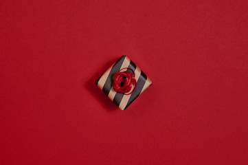 On red background lies a gift wrapped in yellow and black striped paper. In the singular. New year, gift, holidays.