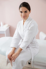 Beautiful young woman sitting on daybed at spa salon
