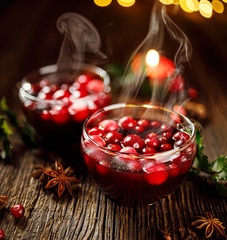 Cranberry mulled wine with aromatic cinnamon, anise and cloves in glass cups on a wooden table....