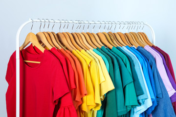 Fototapeta premium Rack with bright clothes on light blue background. Rainbow colors