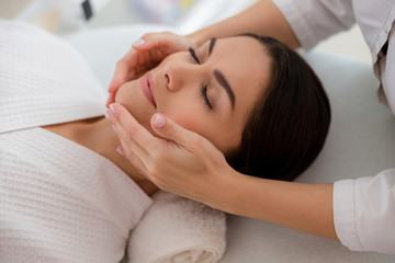 Fototapeta na wymiar Masseuse massaging lady face at beauty salon