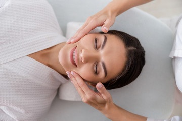 Fototapeta premium Masseuse hands massaging face of smiling lady