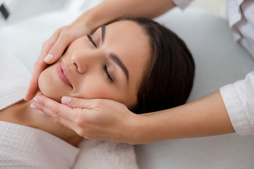 Fototapeta na wymiar Relaxed young woman enjoying face massage at spa salon