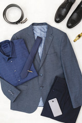 Suit jacket, pants, blue shirt, black shoes, belt, watch, necktie, smartphone. Overhead view of classic elegant formal men's outfit. Set of stylish men's clothes and accessories. Flat lay, top view.