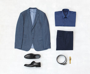 Suit jacket, pants, blue shirt, black shoes, belt, watch on grey background. Overhead view of classic elegant formal men's outfit. Set of stylish men's clothes and accessories. Flat lay, top view.