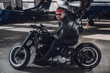 Fototapeta na wymiar Bearded guy having rest on motorcycle in garage