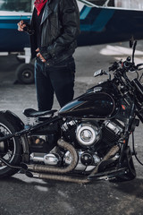 Cropped photo of man in leather clothes standing near motorcycle