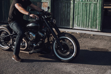 Adult biker sitting on modern motorbike near garage