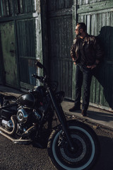 Fototapeta na wymiar Handsome calm biker standing near garage outdoors