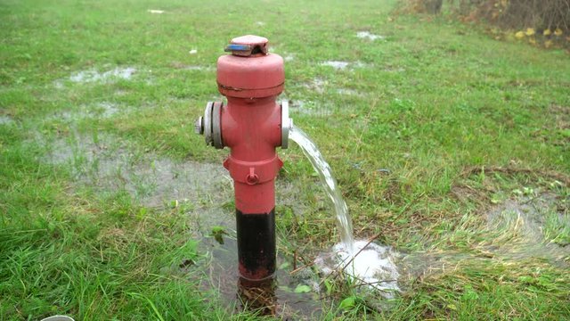Leaking fire hydrant. Red hydrant on the green field is leaking water. Open fire hydrant letting the water flow out on to the grass. Water flowing from red fire hydrant.