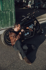 Fototapeta na wymiar Handsome biker is sitting near motorbike outdoors