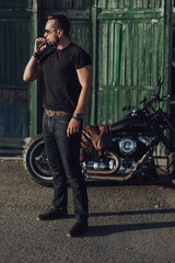 Fototapeta na wymiar Attractive Caucasian guy standing near motorbike and smoking