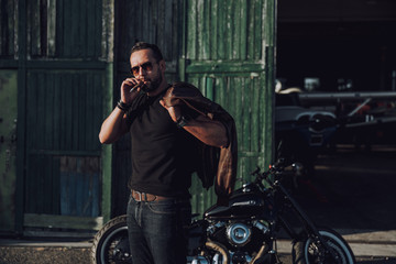 Obraz na płótnie Canvas Caucasian sexy man sitting near motorbike and smoking