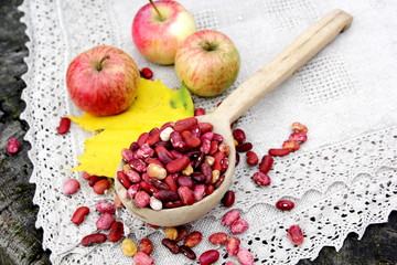 Red beans in wooden spoon putting on linen cloth with autumn apples and yellow maple leaves