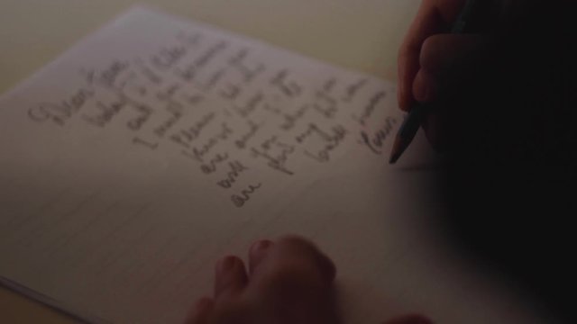 close up su mano che firma una lettera con una matita su un foglio di carta