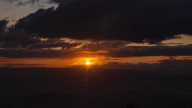 Time lapse of golden sun setting behind dark storm clouds