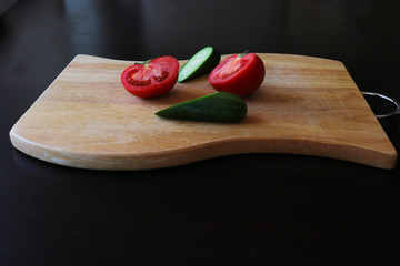 Fresh tomatoes and cucumbers on wooden cutting board on a dark background 