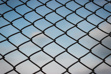 Iron wire mesh fence on a blue sky with white clouds. Chain link fence and blue sky background beyonde and blue sky background beyond.