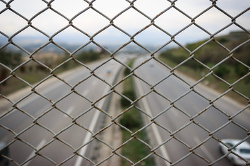 Pattern of wire mesh fence. Highway landscape at background.