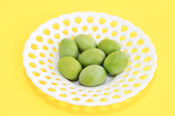 green natural fresh olives in a white decorative plate on a yellow background