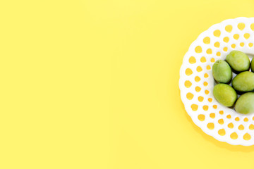 green natural fresh olives in a white decorative plate on a yellow background