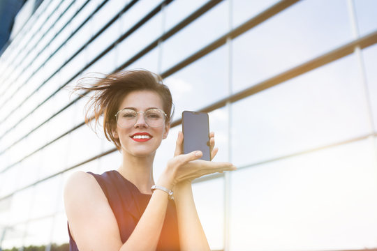 A portrait of young beautiful office woman with bright makeup, red lips, glasses shows a new phone