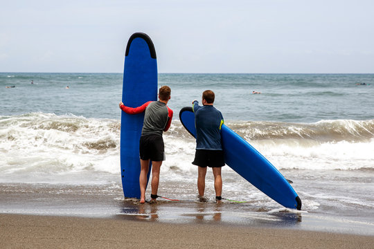 Two men go into the water to learn how to surf.