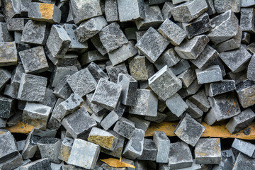 Pile of black natural stone cubes for making outdoor pavement tiles. Chaotic stack of broken road tiles. Construction background of mess geometric backdrop with grey shades pavement stone blocks