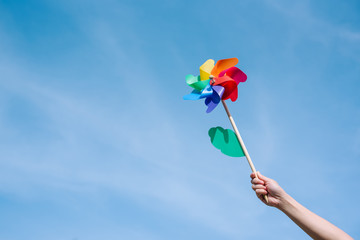 Hand holding pinwheel with blue sky background.