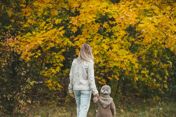 Naklejka na ściany i meble Mother and and little daughter, walking on autumn park. They are talking and enjoying beautiful autumn day.