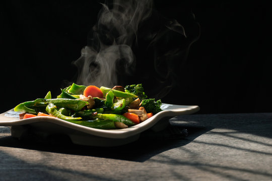 Steam from hot-blanched vegetables in dish on wood table by the window in kitchen with morning sun light,Kale,Mushrooms and Carrots contain vitamins and fiber with good health benefits,Healthy Eating.