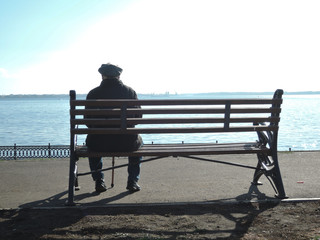 elderly old man sits alone on a bench leaning on a cane and looks into the distance remembering his youth