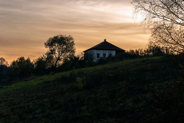 Rural landscape with a silhouette of a hut on a hill on the background of a sunset cloudy sky