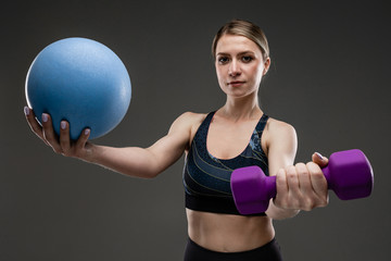 Young sports girl with long blonde hair sealed in tail, beautiful appearance, sports body, in top and legins, holds sports equipment, gantel and ball © Ivan Traimak