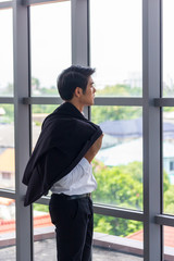 A young Asian businessman looks out of the window. Along with removing the outer jacket