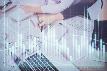 A woman hands writing information about stock market in notepad. Forex chart holograms in front. Concept of research. Double exposure