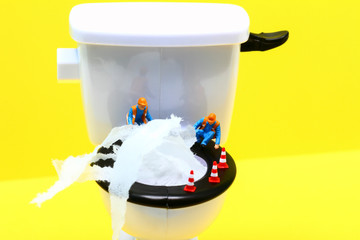 Conceptual image of a miniature figure workmen surveying a blocked toilet overflowing with tissue...